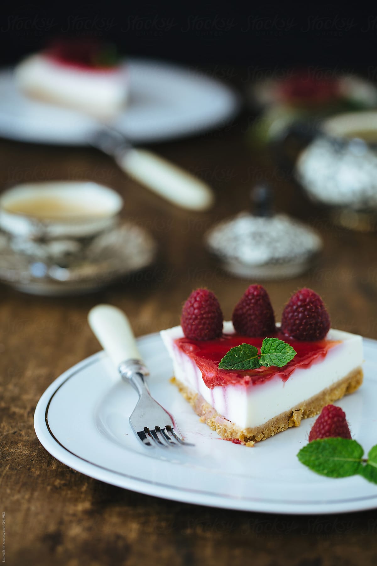 Slices of raspberry cheescake with mint on them on table with coffee cups