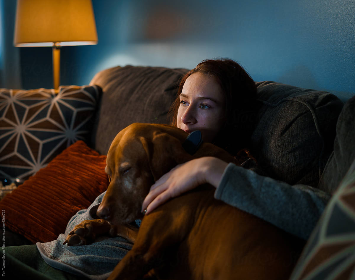 A young white woman relaxes on the couch with her dog