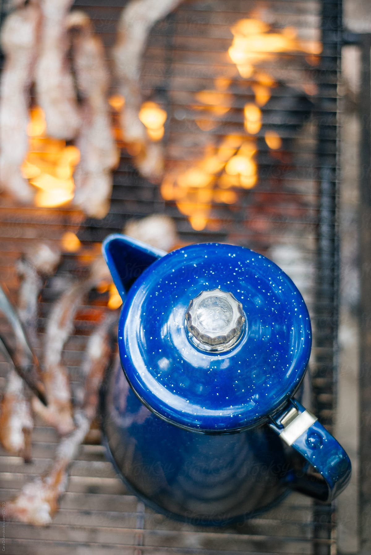 Coffee pot warms on a campfire while bacon cooks beside it