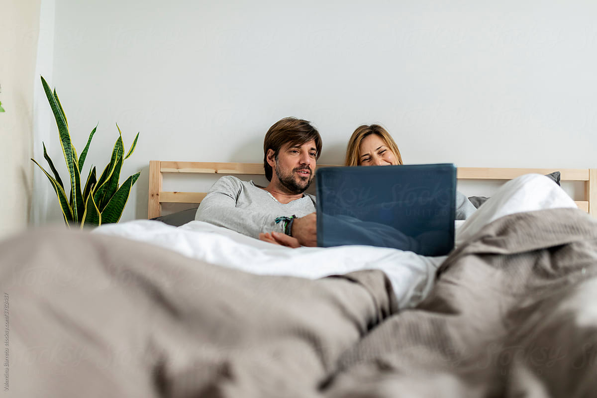 Couple In Bed Using Laptop For Wifi Entertainment