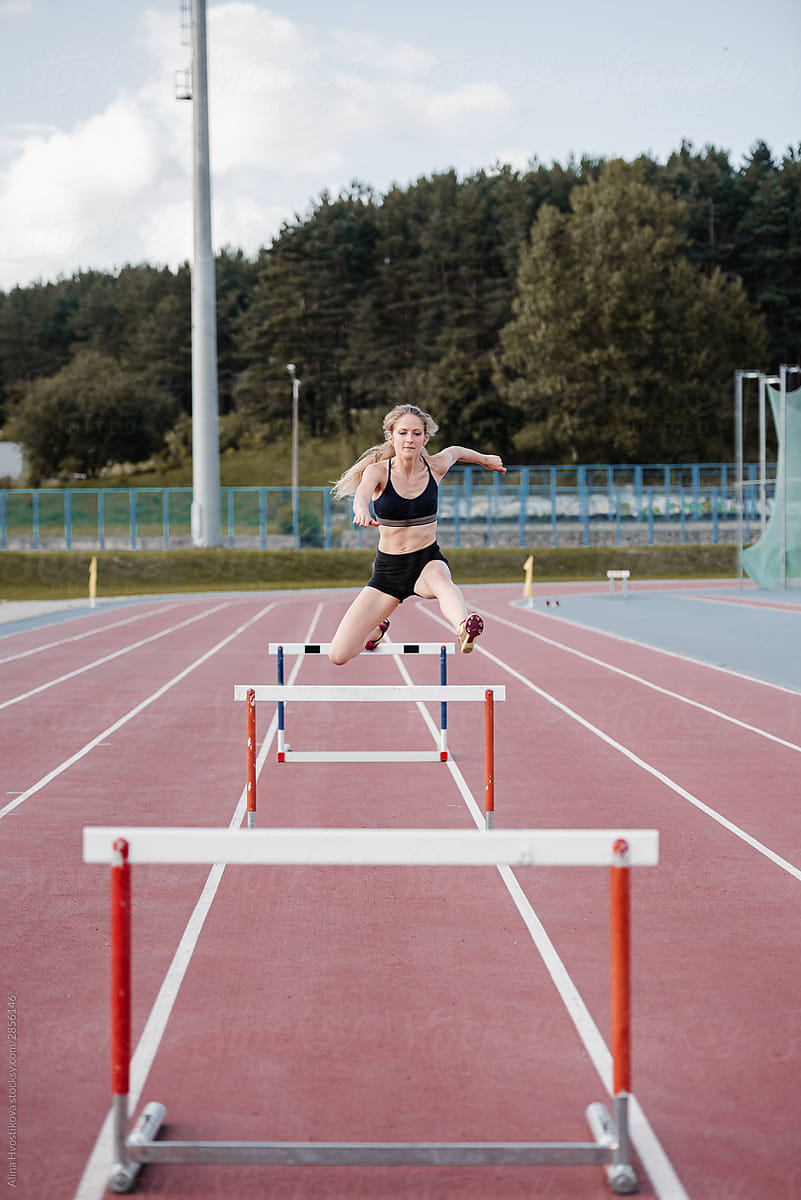 Female athlete leaping over barrier at stadium