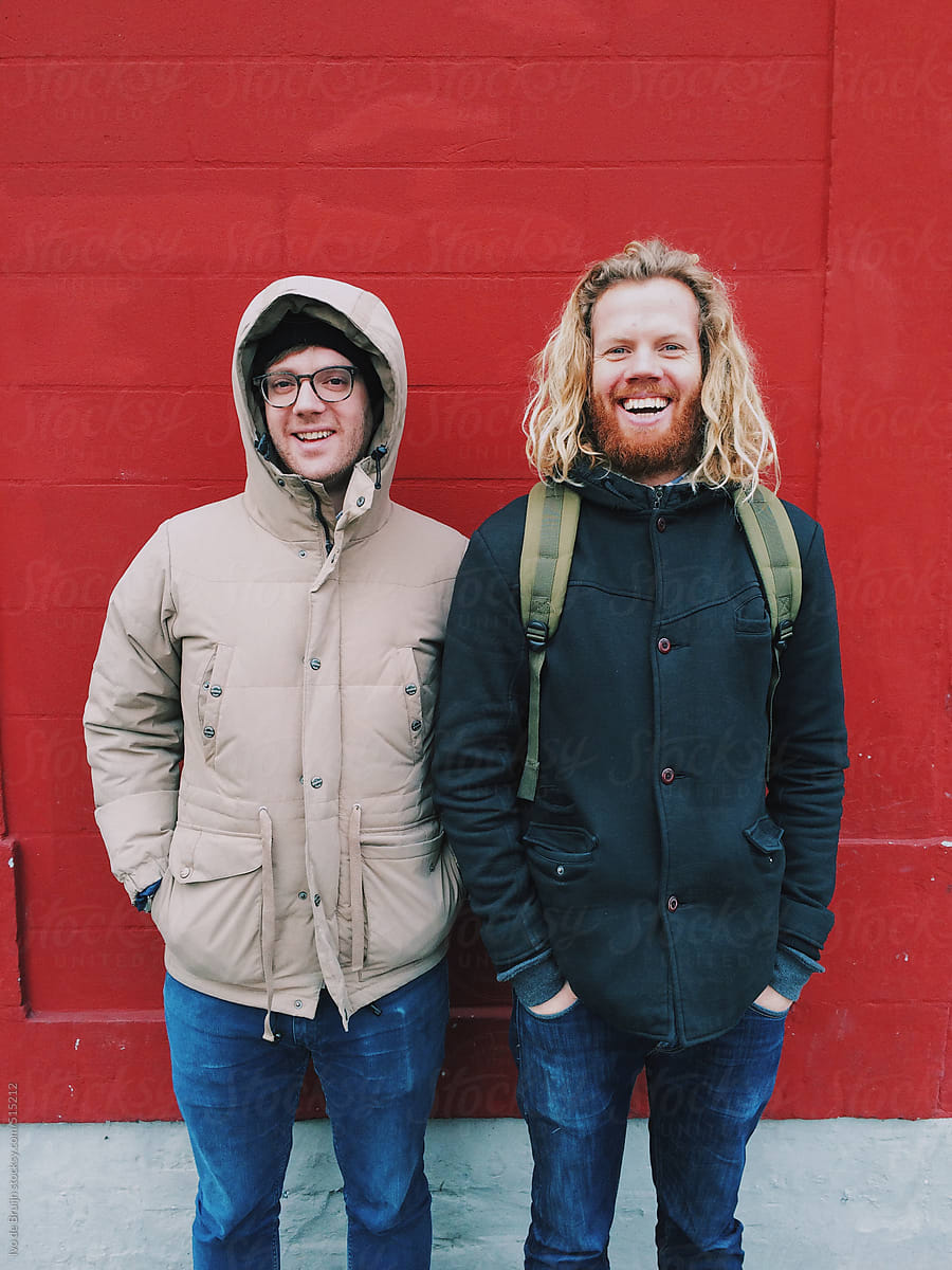 Two good smiling friends in warm jackets standing in front of a red wall