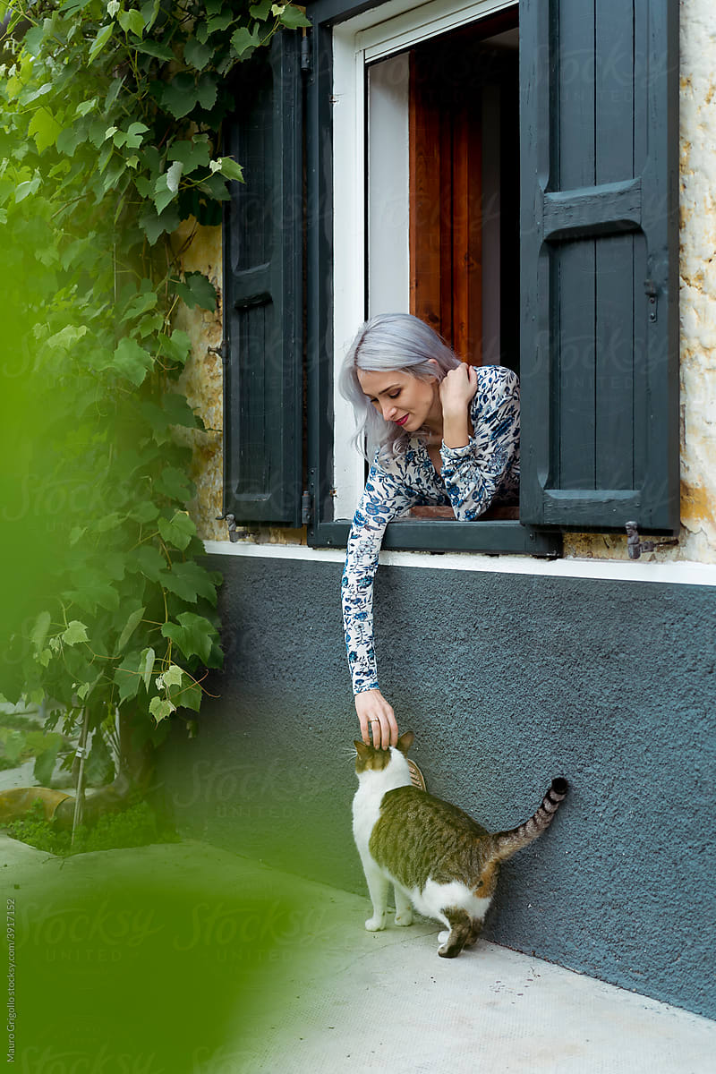 A woman at the window is caressing her friendly cat