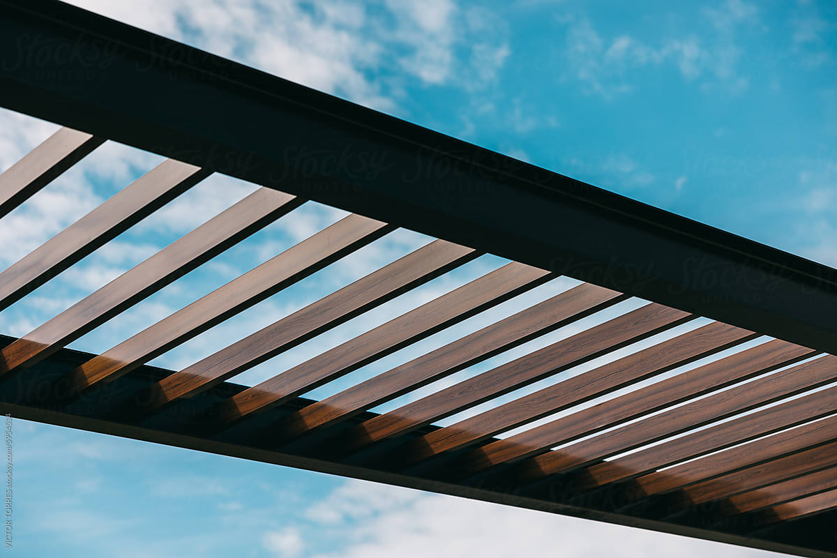 Modern wooden pergola against a blue sky with clouds