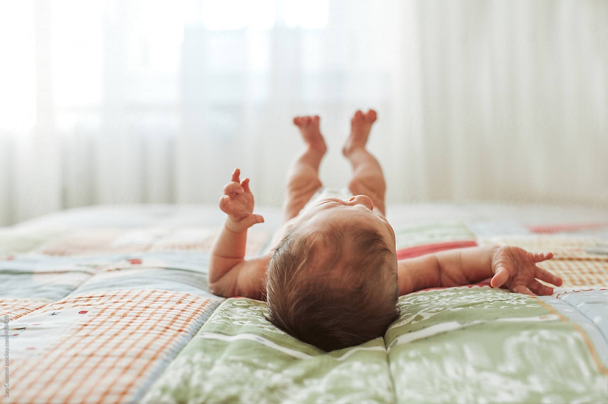 Newborn baby awake lying and stretching on a quilt blanket