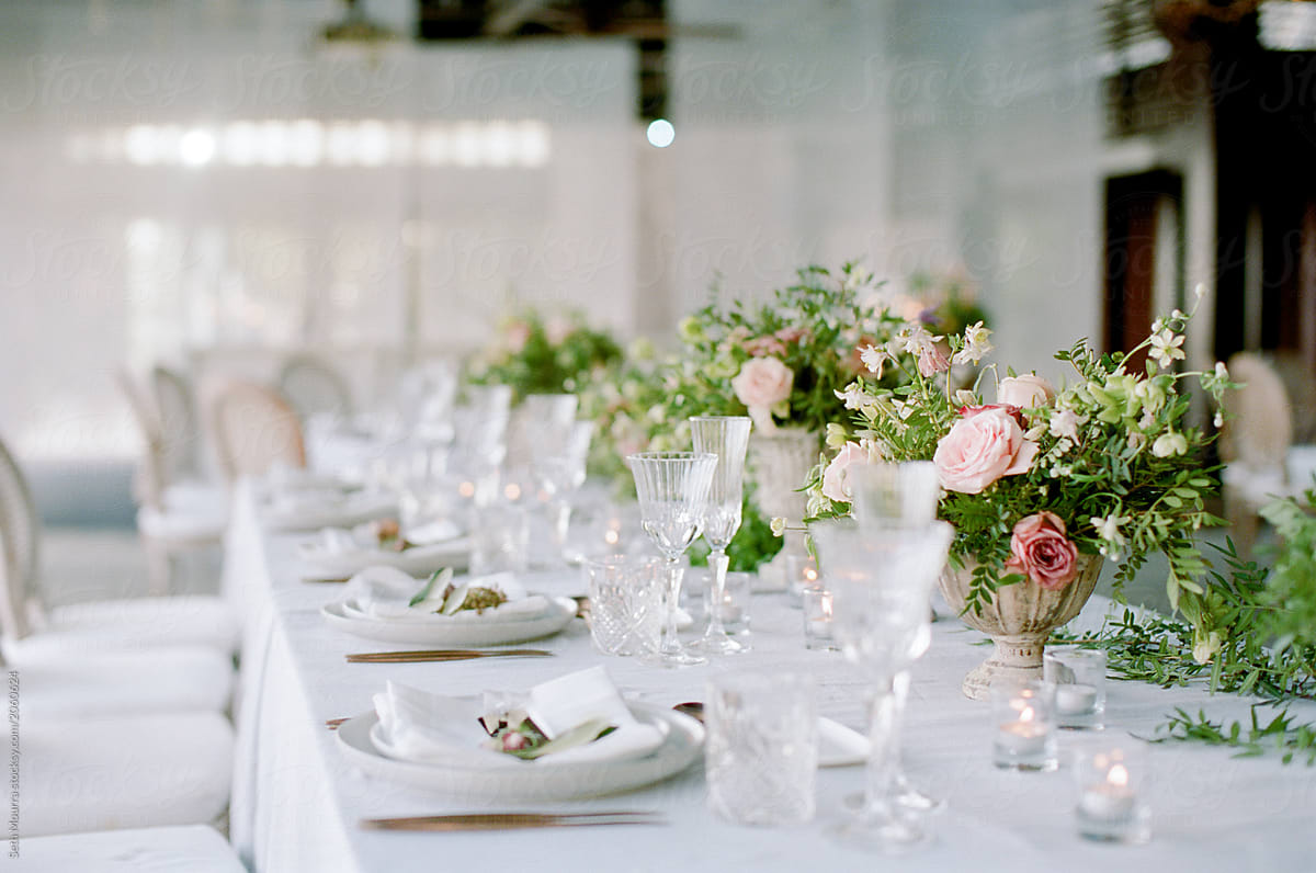 A wedding reception tabletop decorated with neutral linens, floral arrangements & glassware