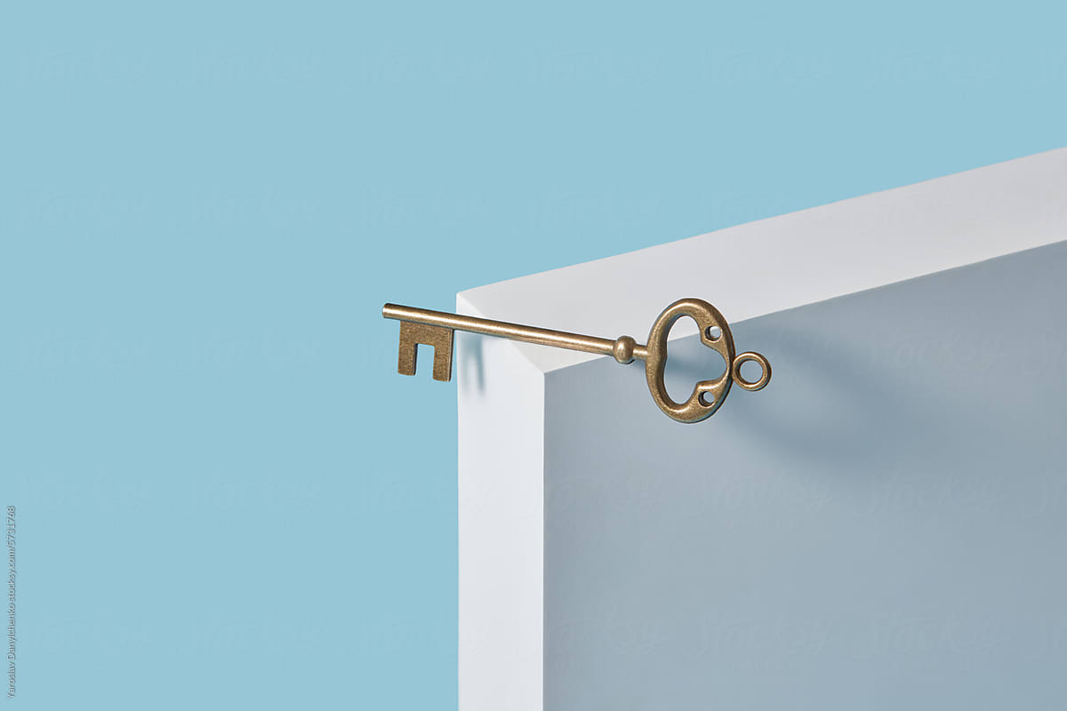 Golden old style door key lying on edge corner of white stand