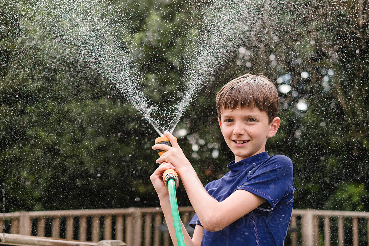 Happy child plays with a water hose in the garden