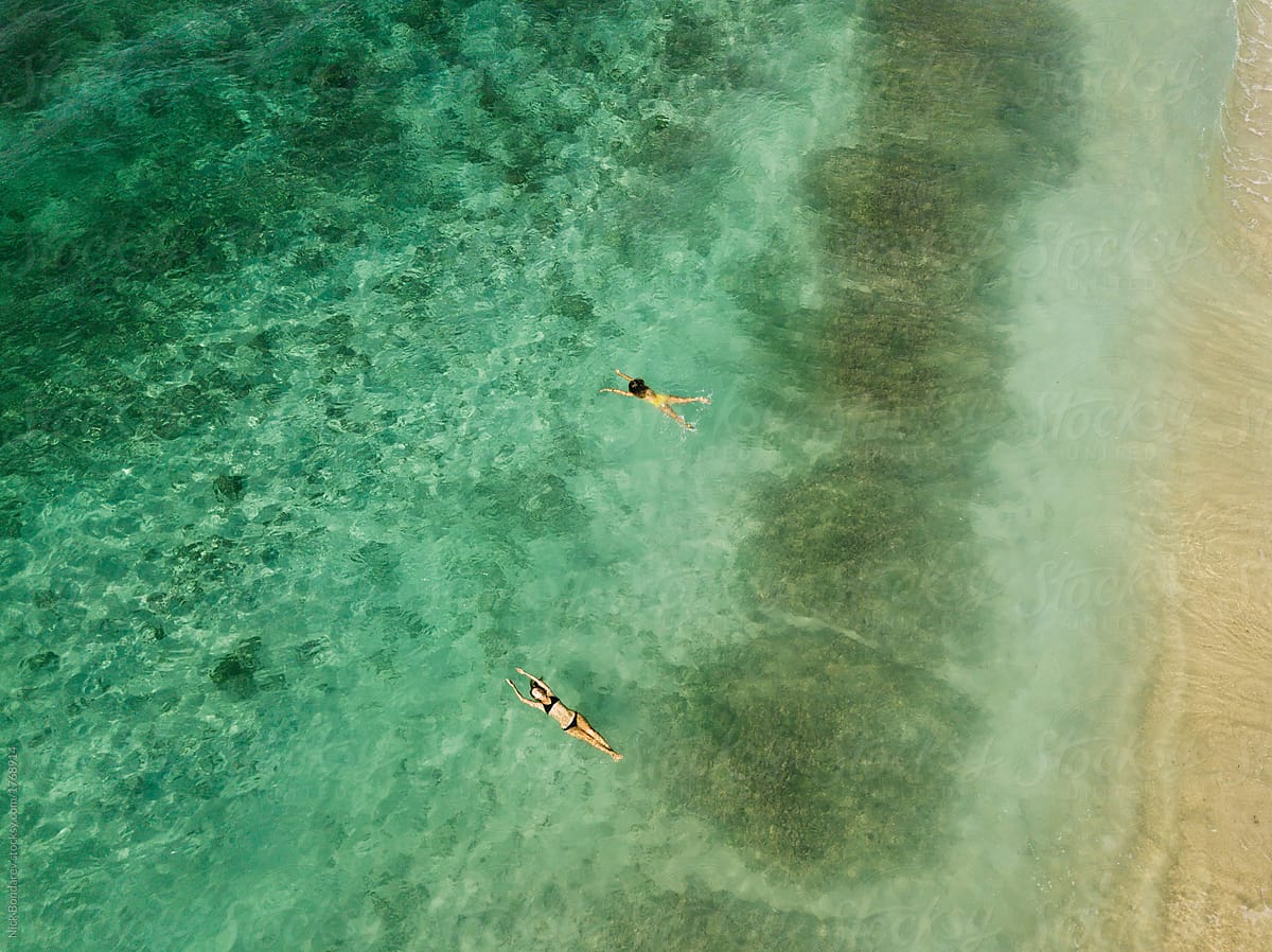 two persons, couple swimming together in the clear green ocean view from above,