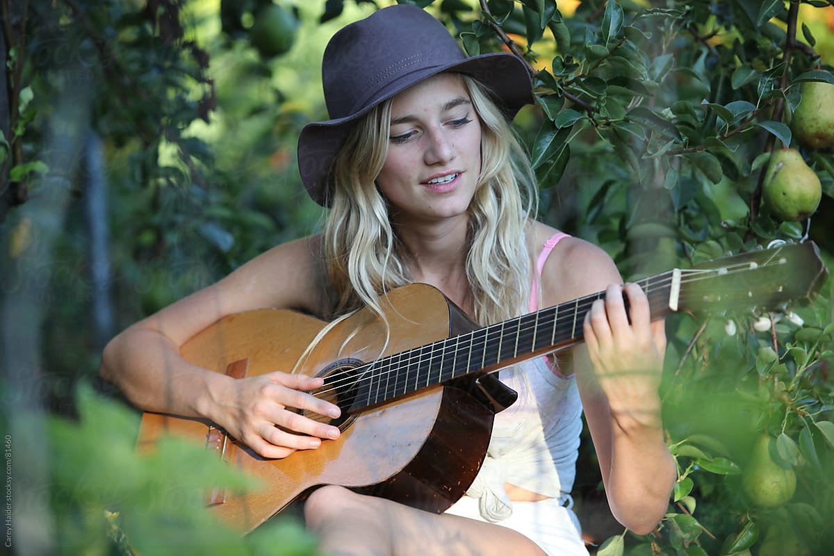 A Youthful Young Beautiful Woman Playing Guitar In A Garden