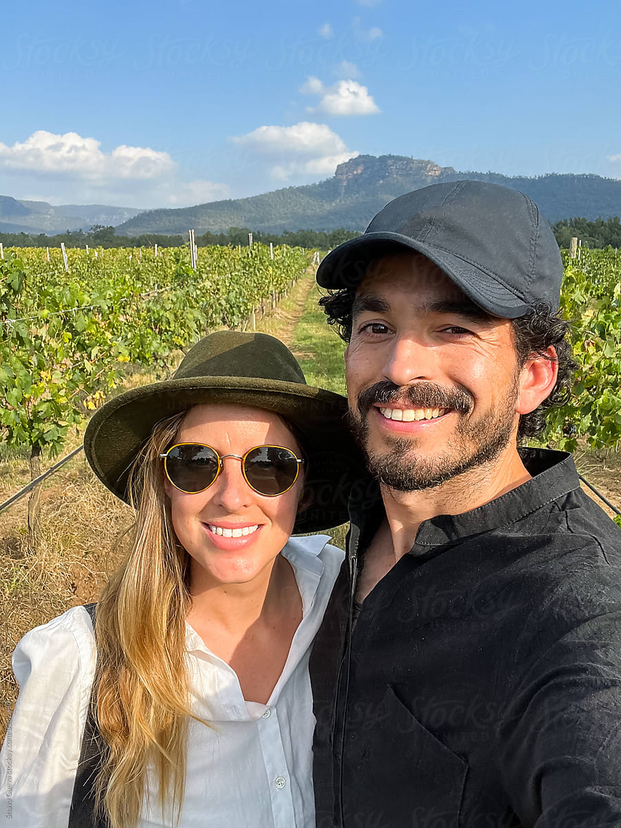 A smiling couple taking a selfie in front of some vineyards