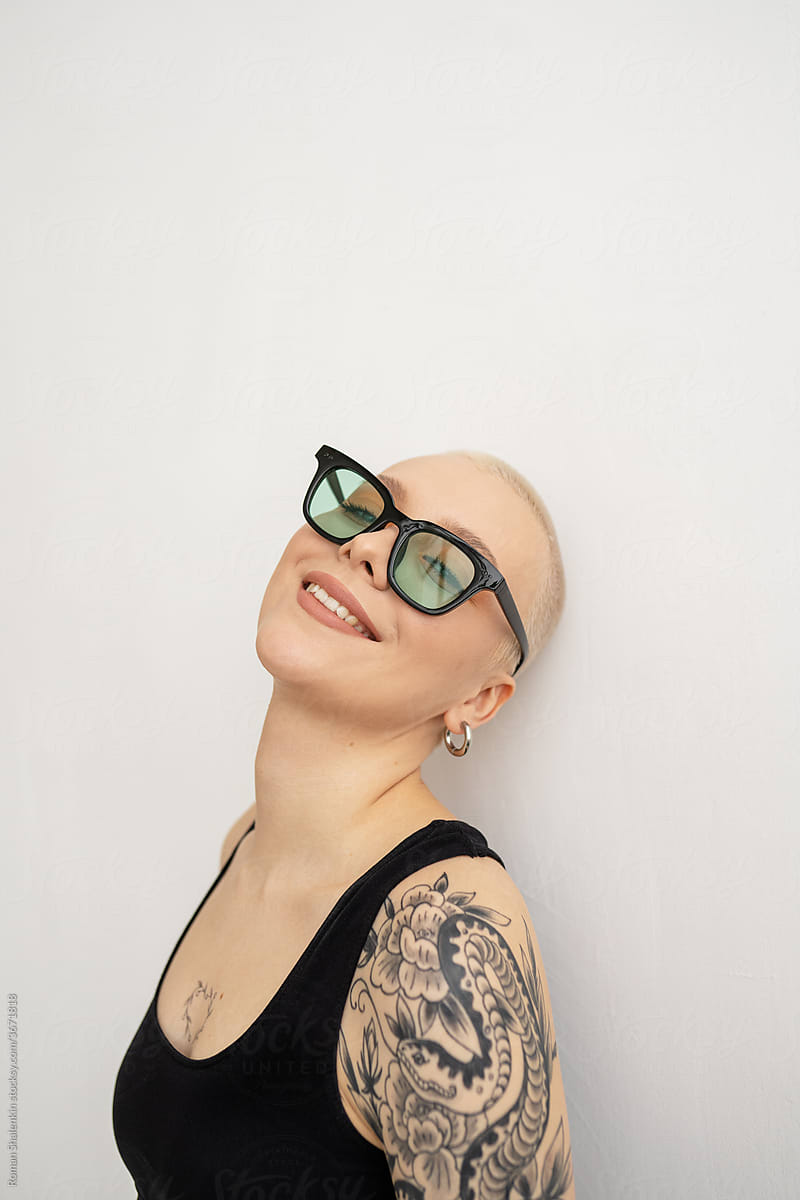 Portrait cheerful sexy informal young woman with short hair and tattoo in turquoise glasses