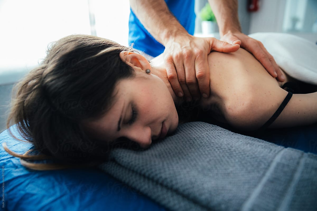Relaxed young woman lying on her front on a bed receiving a massage on her back by a male therapist