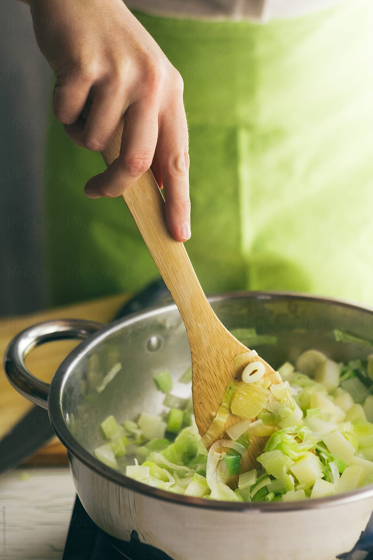 Woman stirring leeks, potato and onion in pan to make soup