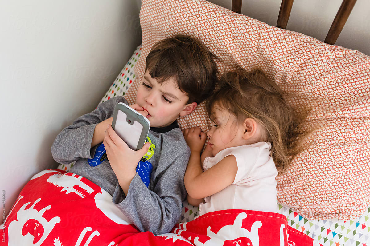 boy watches video on smart phone while sister sleeps