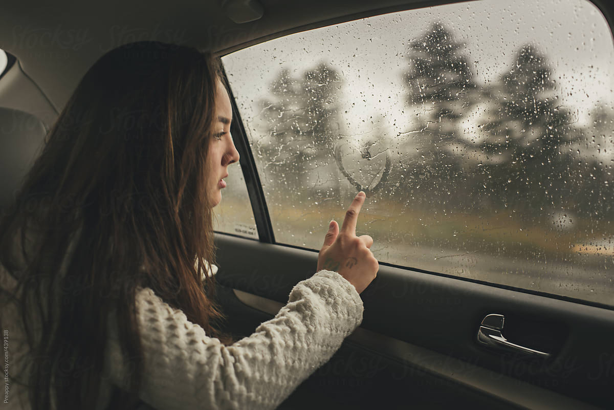 Teenage girl drawing a heart shape on a car window