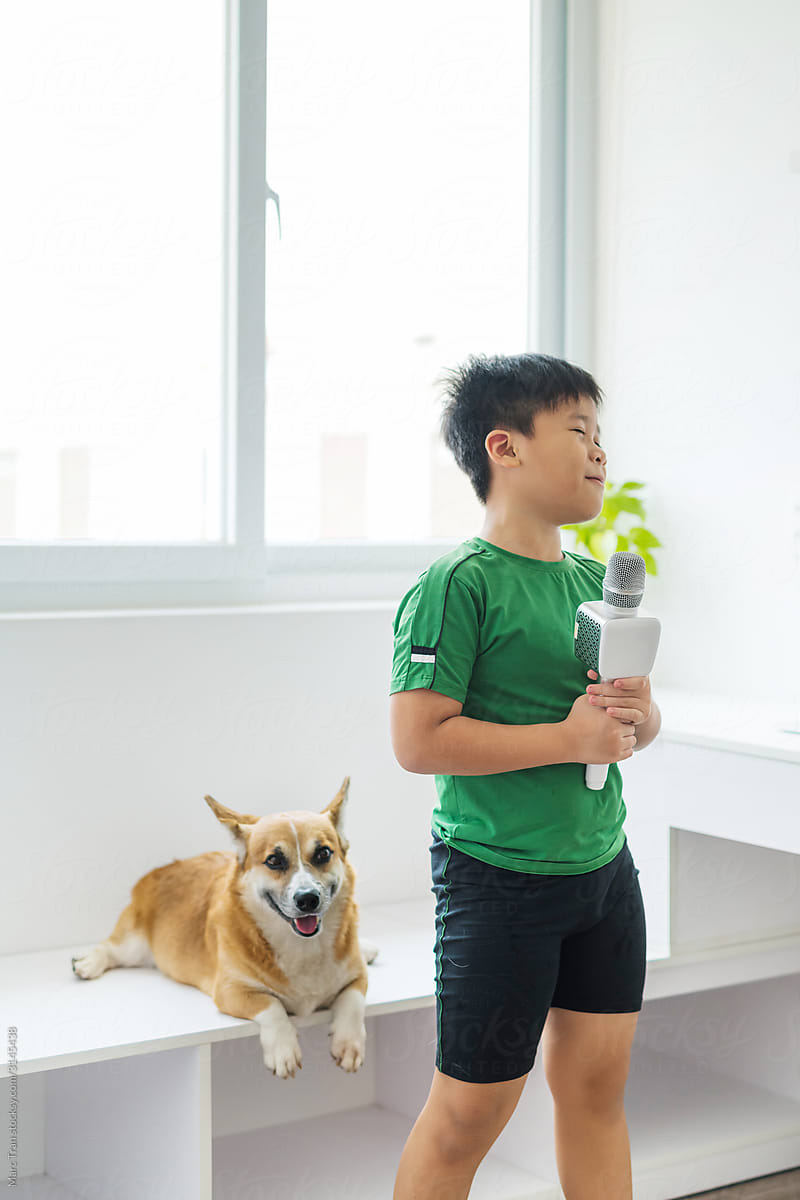 Happy boy singing karaoke with corgi dog at home