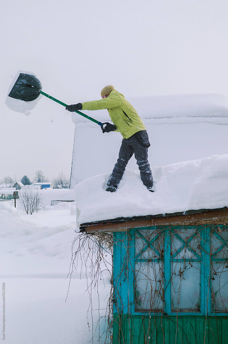 Man in yellow down jacket shovels snow off roof