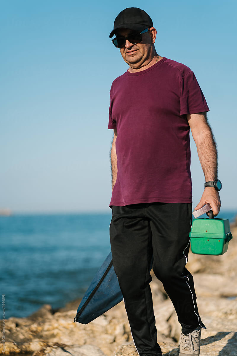 Smiling fisherman strolling at seaside with tackle box