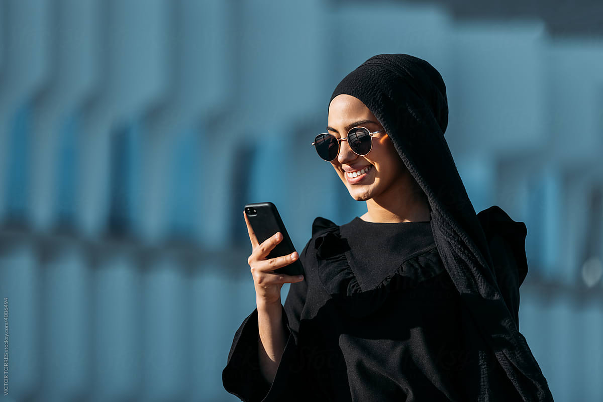 Elegant Muslim woman in stylish outfit using cellphone on street