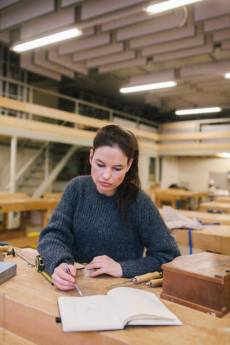 Female woodworker working behind a workbench and looking at her notebook for notes