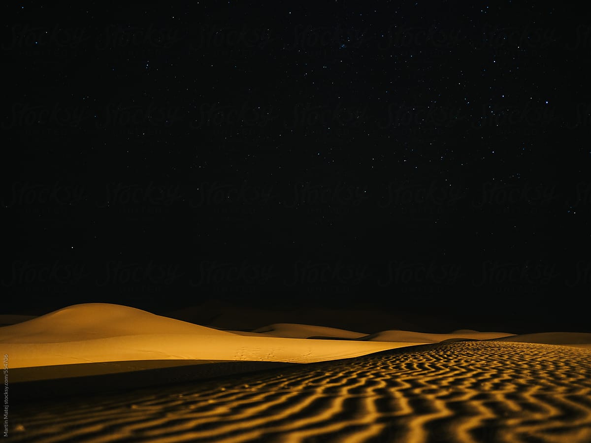 Lines in the sand leading to a dune at night