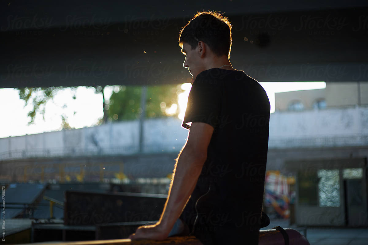 photo of a guy in a black T-shirt with backlight against a skatepark