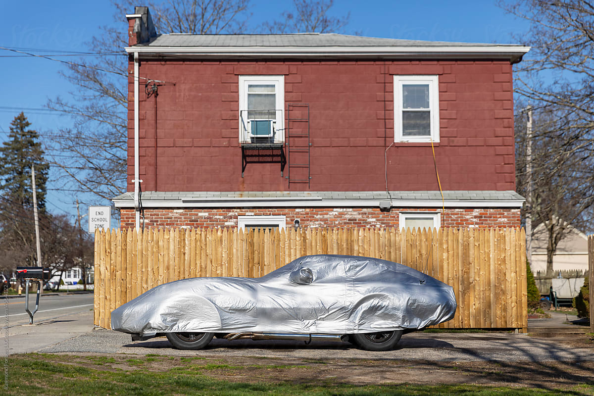 Sports Car covered with silver protective cloth in driveway