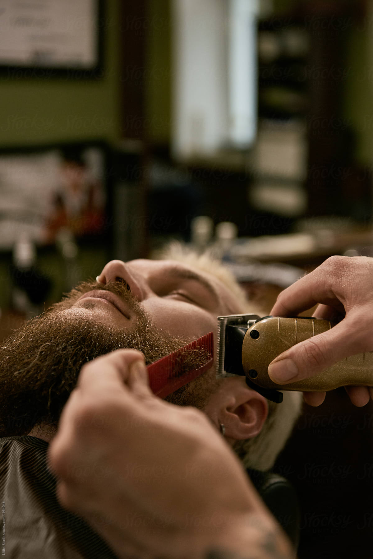 Crop barber trimming beard of man