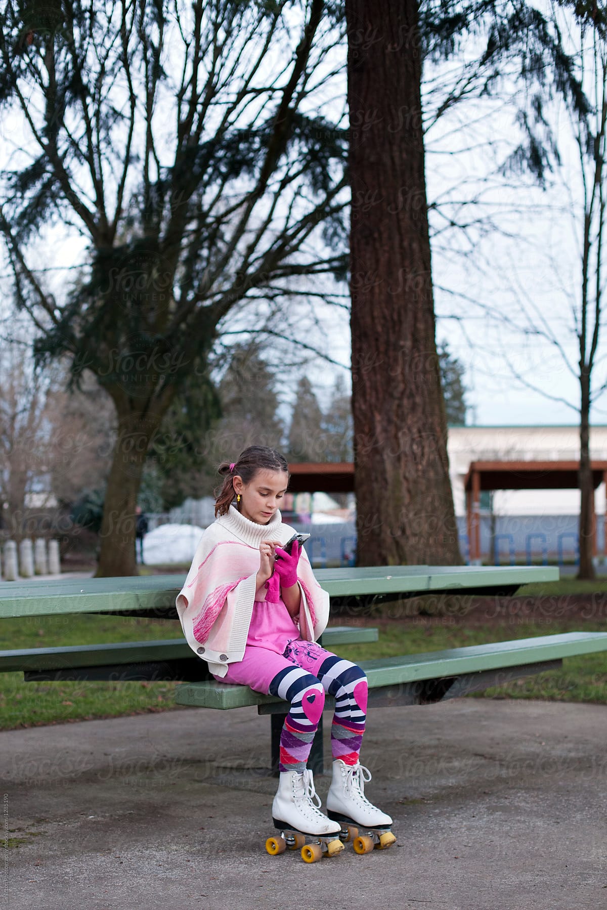 Preteen girl wearing roller skates using smartphone while seated on a picnic table bench in the park