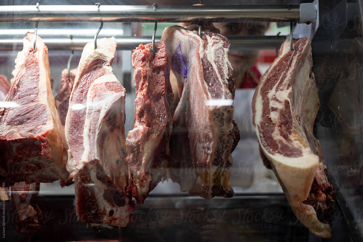 Marbled chunks of meat hanging from hooks: blurred butcher behind them