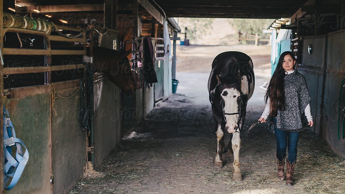 Woman walking horse through stable
