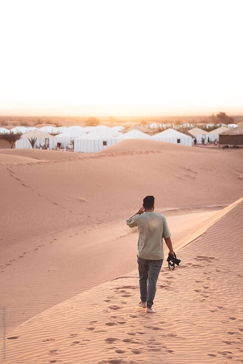 traveler with camera walking at dawn in the desert dunes.