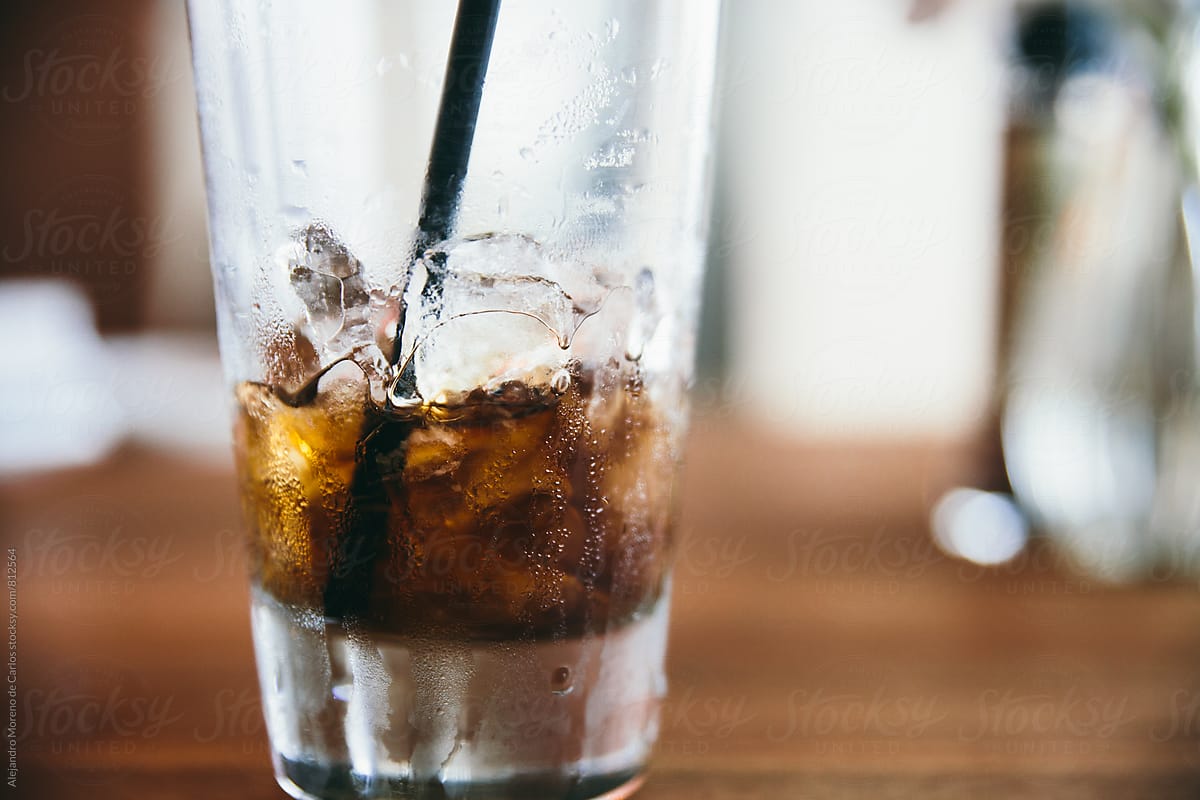 Close up of a soft drink in a glass with ice half finished with a straw inside