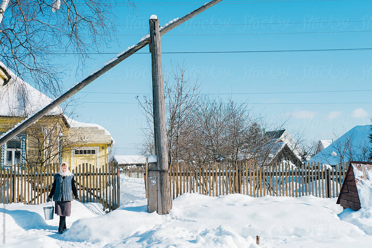 Woman with bucket walking near fence in winter