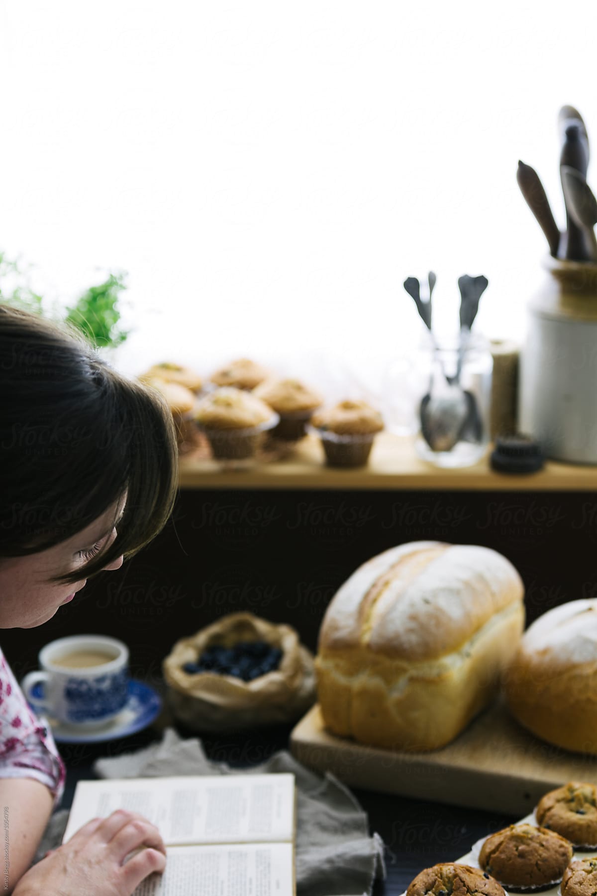 Woman reads old cookery book while bread and muffins cool