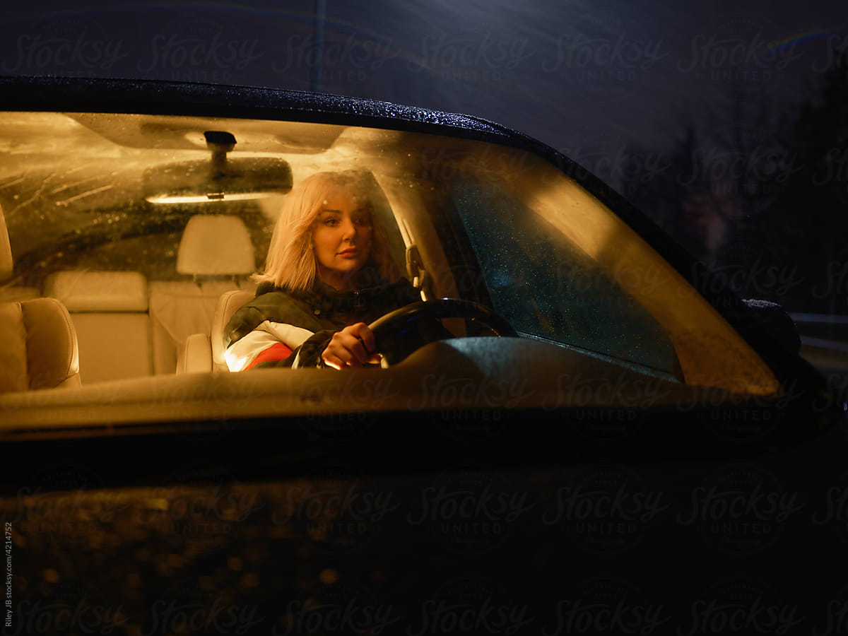Lone woman driver sits in car at night.