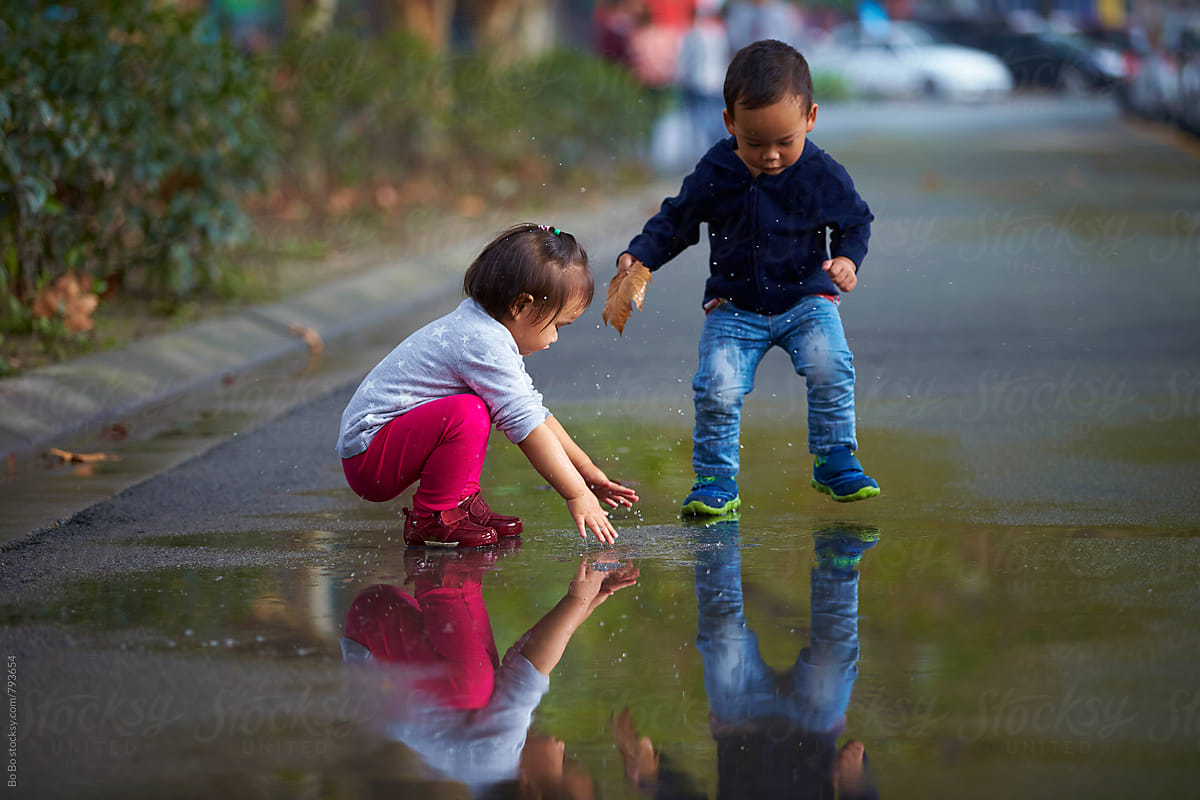 two kids playing the water in the road after rain