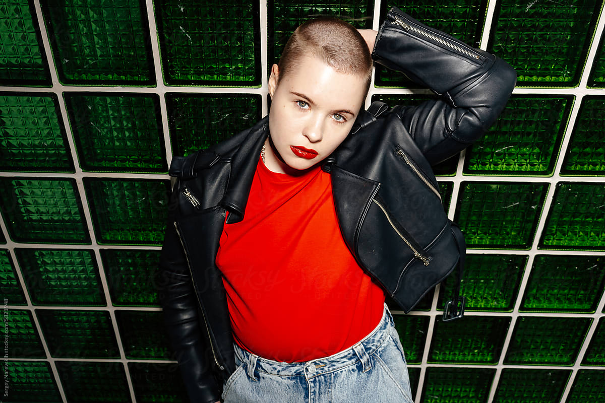 Young female with shaved head at green wall