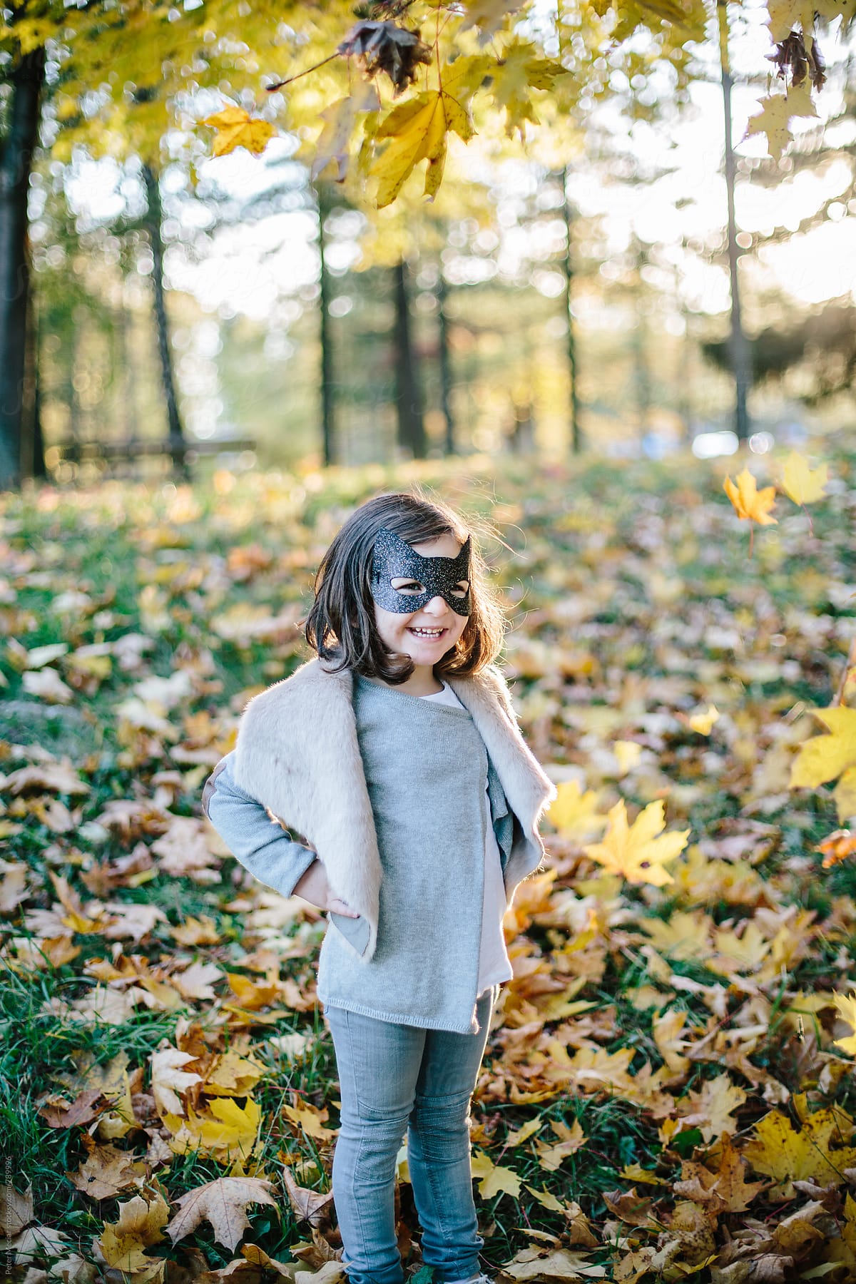 Little girl with a face mask is playing in autumn park and throw autumn leaves