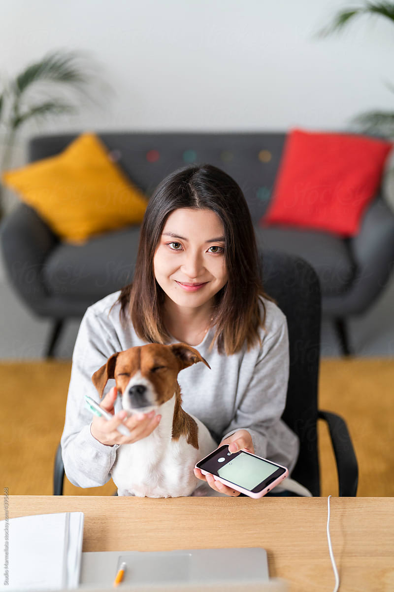 Smiling Asian woman with smartphone caressing dog