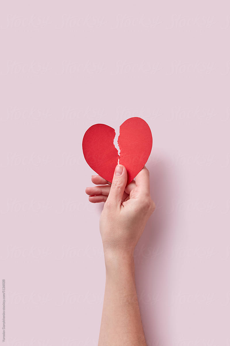 Red ripped paper cut heart held by female hand.