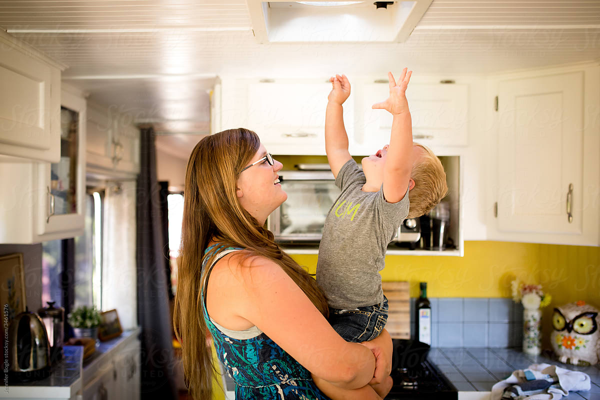 Smiling Mother holds toddler as he reaches to the ceiling