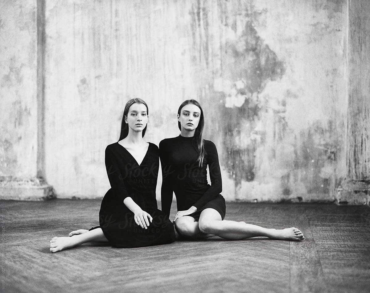 Two Slim Young Women Wearing Dresses Sitting on Wooden Floor