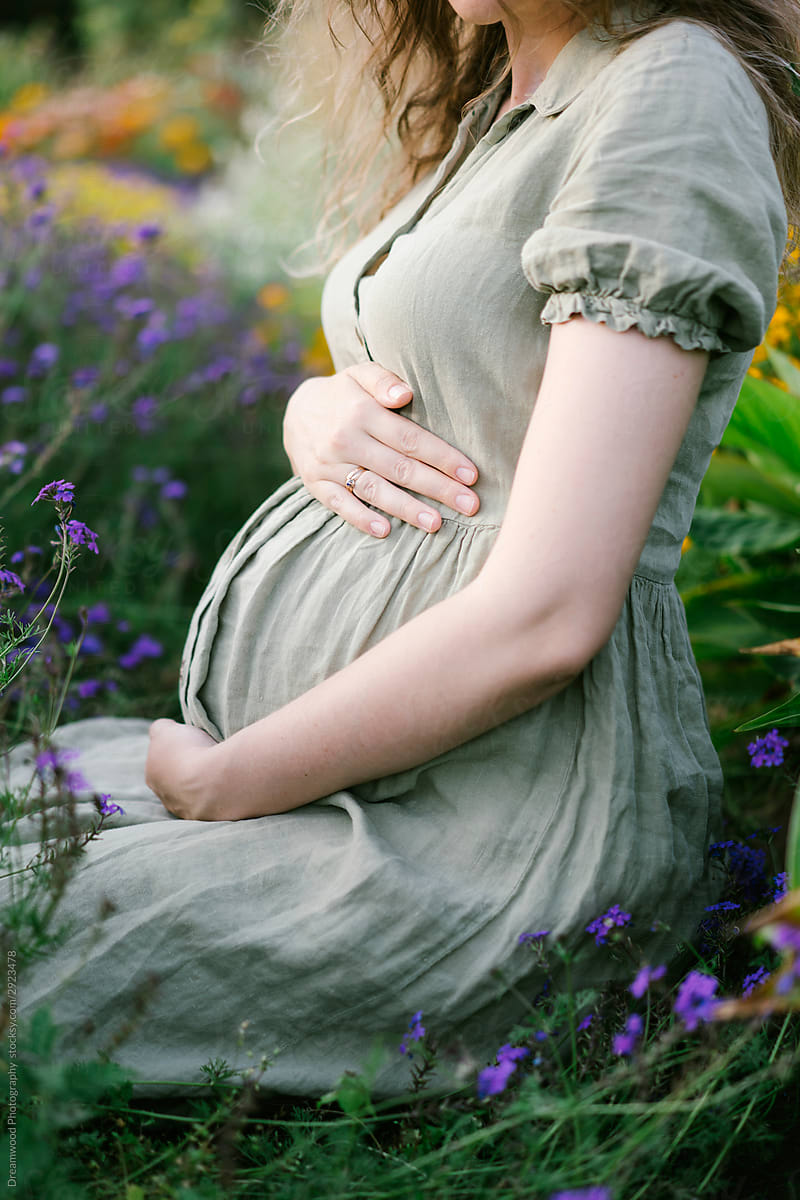 Pregnant woman resting in blooming meadow in sunny day
