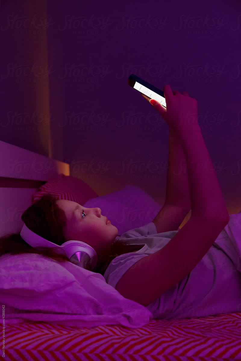 Girl with smartphone relaxing on bed at night