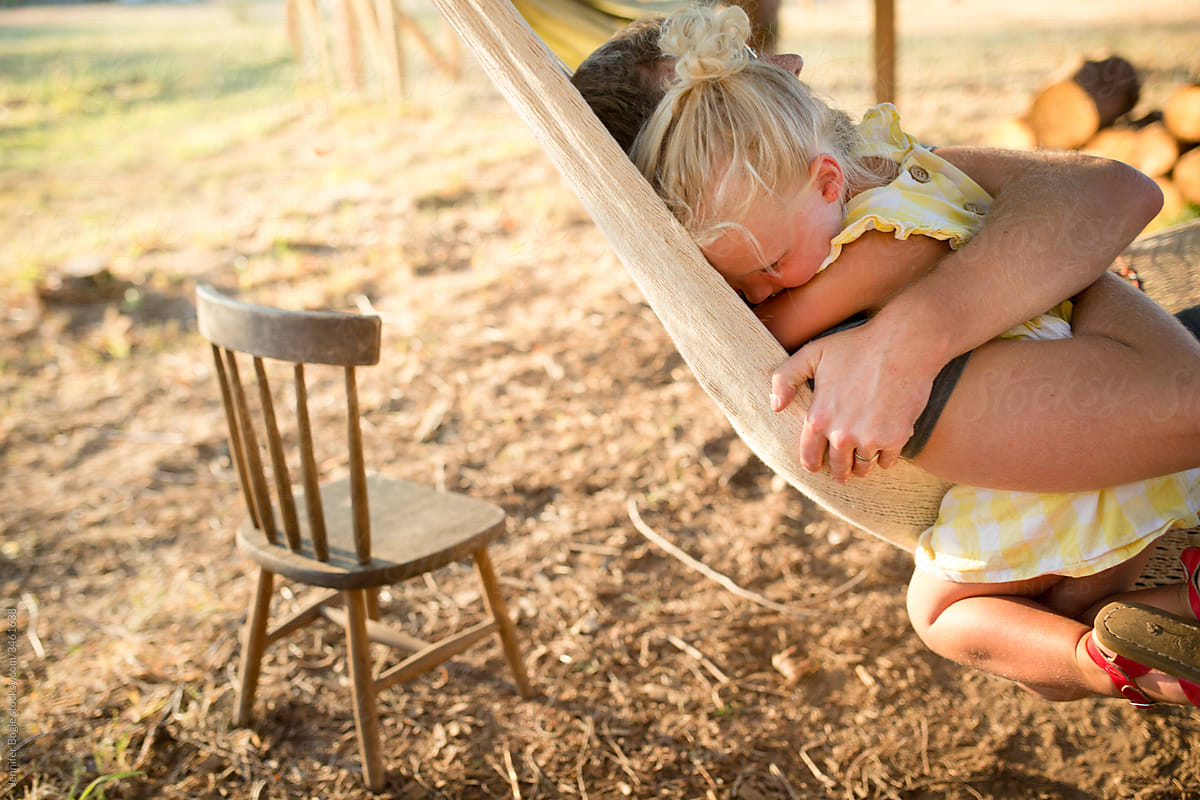 Father tightly hugs young daughter in hammock