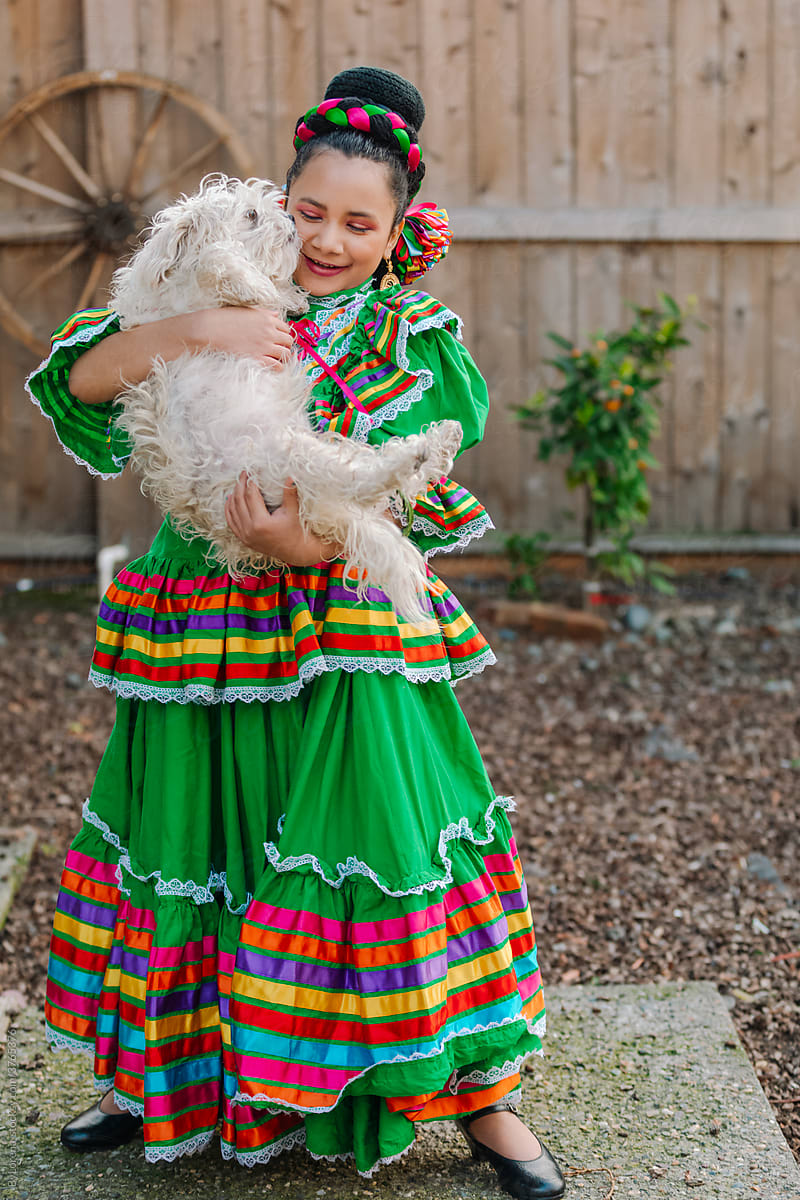 Girl wearing traditional Mexican dress hugging dog