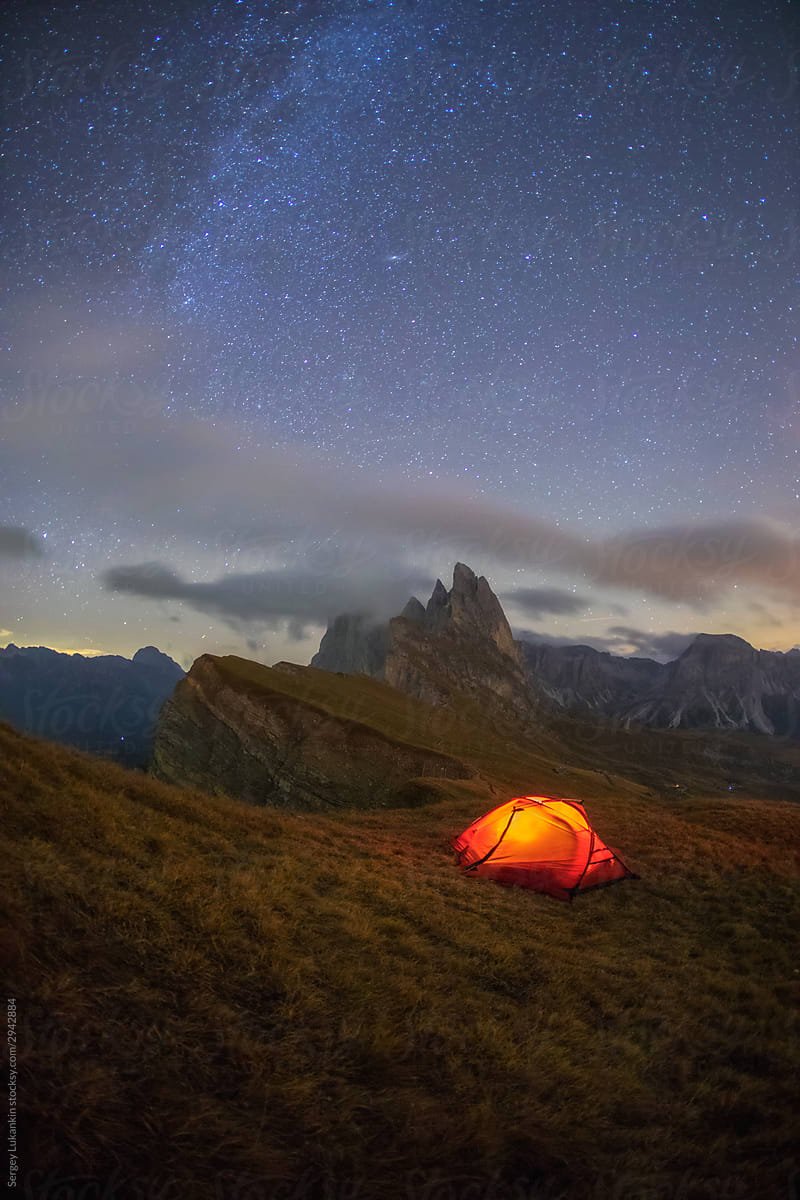 A tent on the edge of a cliff under a starry sky with a mountain in the background