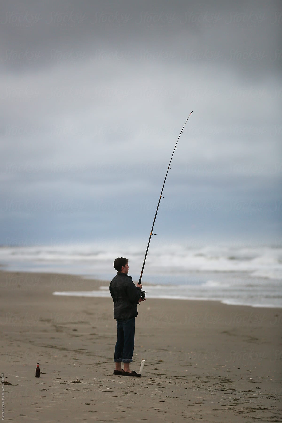 Man waiting and surf fishing with long rod and beer on beach